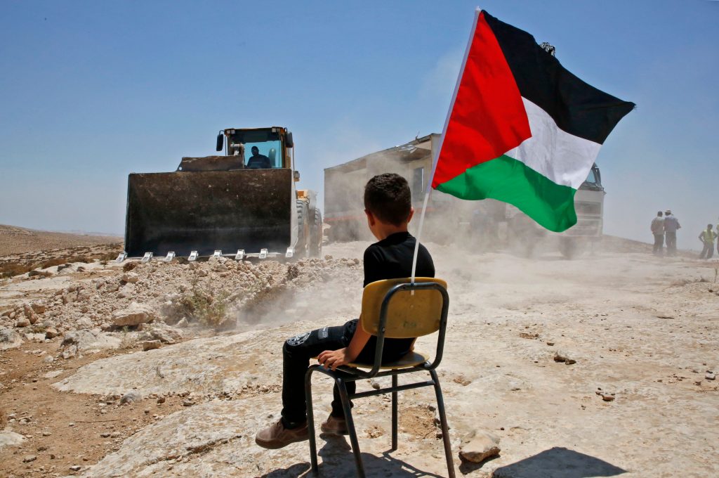 TOPSHOT - A Palestinian boy sits on a chair with a national flag as Israeli authorities demolish a school site in the village of Yatta, south of the West Bank city of Hebron and to be relocated in another area, on July 11 2018. (Photo by HAZEM BADER / AFP)        (Photo credit should read HAZEM BADER/AFP/Getty Images)