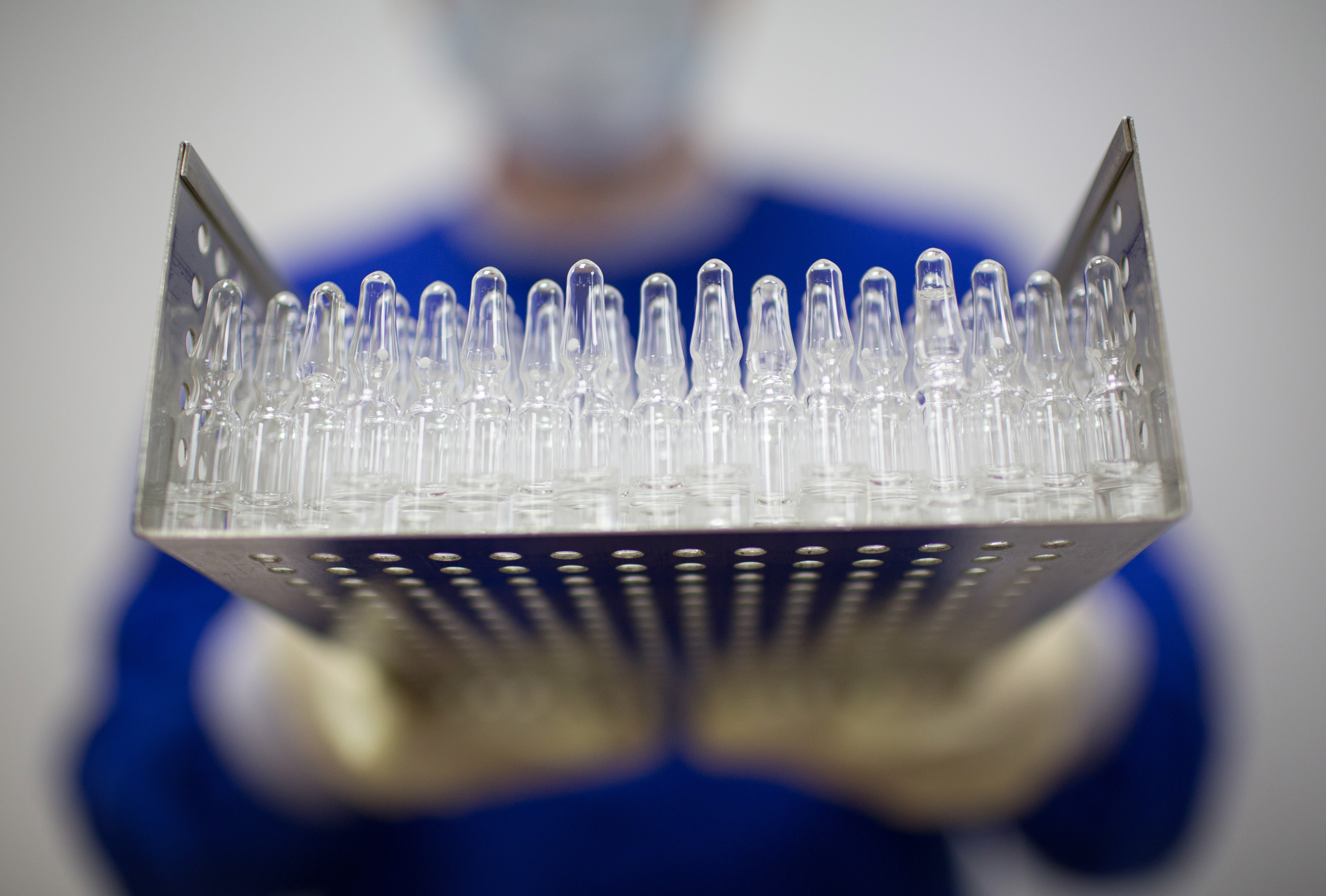 A worker wearing personal protective equipment (PPE) holds a tray containing unlabeled ampoules of the 'Gam-COVID-Vac' COVID-19 vaccine, developed by the Gamaleya National Research Center for Epidemiology and Microbiology and the Russian Direct Investment Fund (RDIF), at JSC Binnopharm pharmaceutical complex, operated by Sistema PJSFC, in Zelenograd, Russia, on Friday, Aug. 7, 2020. Russia registered its first coronavirusÂ vaccine, developed by the Gamaleya Institute and the Russian Direct Investment Fund, President Vladimir Putin said during a televised meeting with the government. Photographer: Andrey Rudakov/Bloomberg via Getty Images